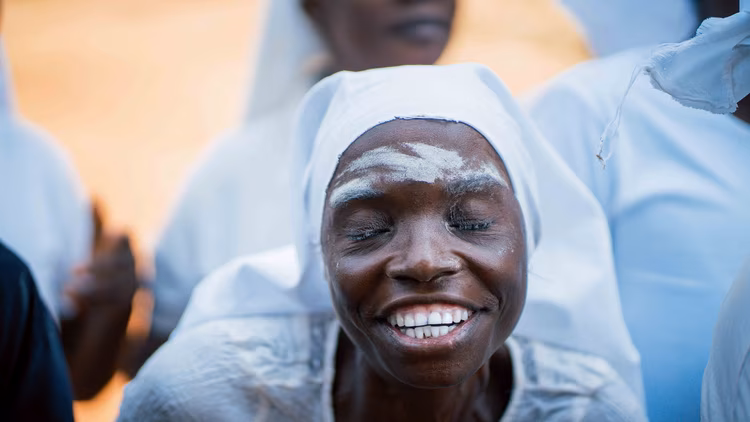 Women draped in swathes of white cloth sweep in waves, ululating between verses; their harmonies and songs urge the drums and crowd forward. (Image by Chona Mweemba for Nkwazi Magazine).