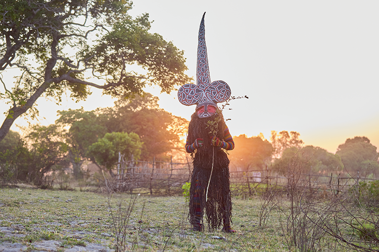 Likishi Chikuza attains total perfection in his duties. With his long conical mitre, his main function is to teach tundanji the art of the kuhunga dance, until perfected. (Image by Nkwazi/Justine Kunda).